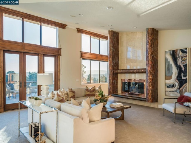 living room featuring a tiled fireplace, plenty of natural light, light colored carpet, and french doors