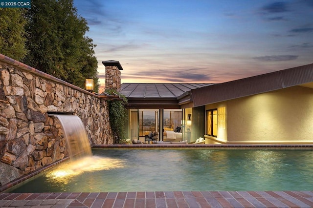 pool at dusk with pool water feature and a patio