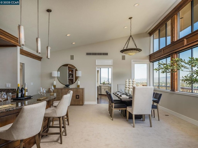 dining area with light carpet, high vaulted ceiling, a healthy amount of sunlight, and indoor bar