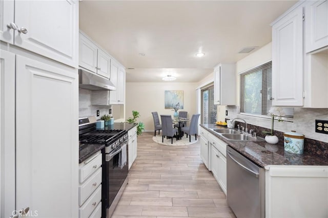 kitchen with white cabinets, stainless steel appliances, dark stone countertops, sink, and light wood-type flooring