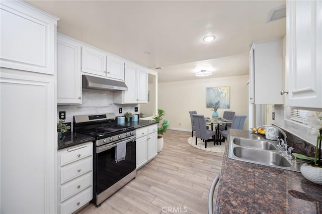 kitchen with dark stone countertops, sink, light wood-type flooring, stainless steel gas range, and white cabinets