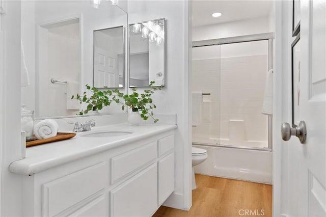 full bathroom with bath / shower combo with glass door, wood-type flooring, vanity, and toilet