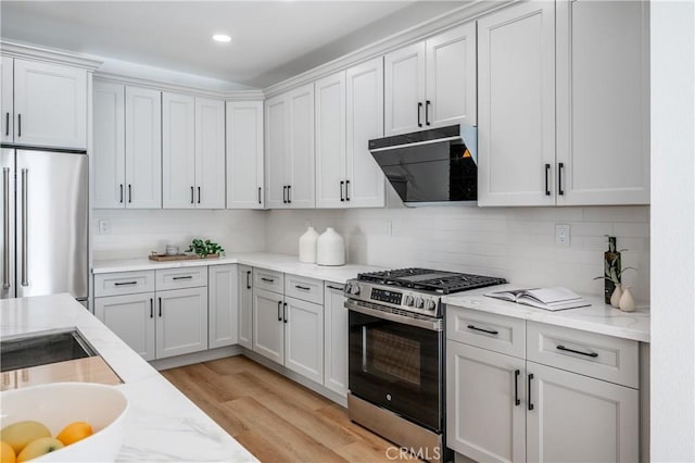 kitchen featuring extractor fan, stainless steel appliances, light hardwood / wood-style floors, decorative backsplash, and white cabinets