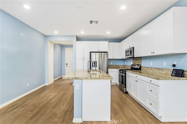 kitchen featuring light hardwood / wood-style floors, white cabinetry, a kitchen island with sink, appliances with stainless steel finishes, and light stone counters