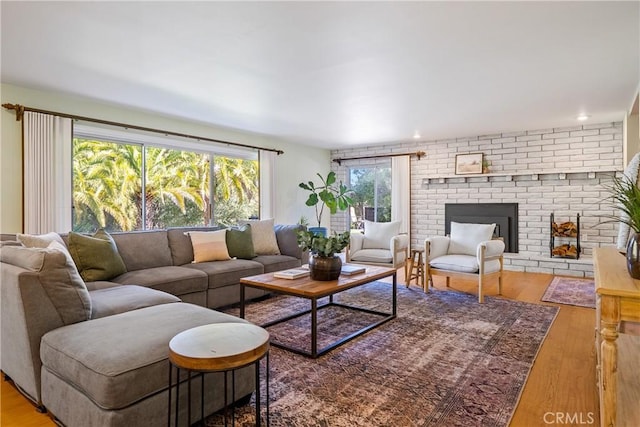 living room featuring wood-type flooring, a brick fireplace, and a wealth of natural light