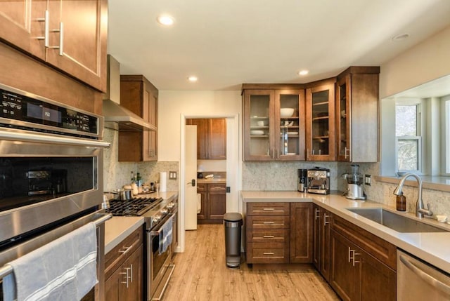 kitchen with sink, wall chimney range hood, appliances with stainless steel finishes, decorative backsplash, and light wood-type flooring