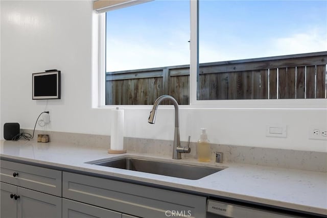 kitchen featuring stainless steel dishwasher, light stone countertops, sink, and gray cabinets