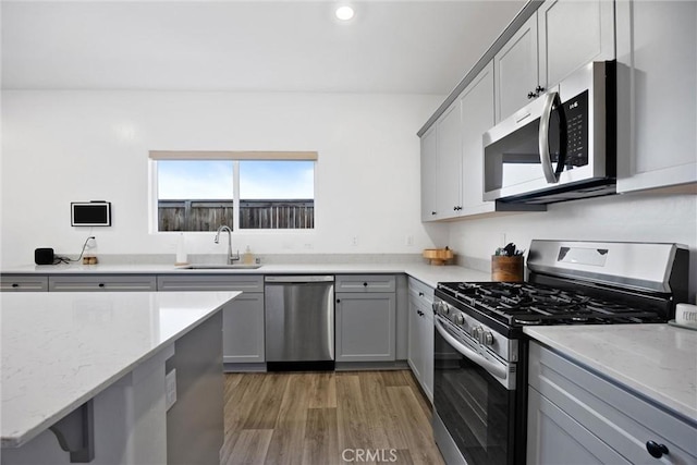 kitchen featuring appliances with stainless steel finishes, sink, light stone counters, and gray cabinets