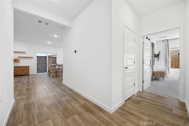 corridor featuring wood-type flooring, beam ceiling, and a barn door