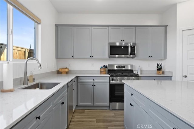 kitchen with light stone countertops, gray cabinets, stainless steel appliances, and sink