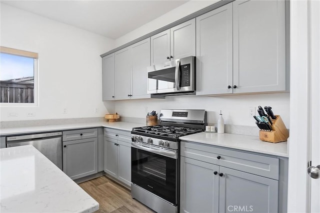 kitchen featuring light hardwood / wood-style floors, light stone counters, gray cabinets, and stainless steel appliances