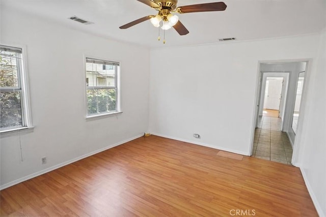 unfurnished room featuring light wood-style floors, baseboards, visible vents, and a ceiling fan