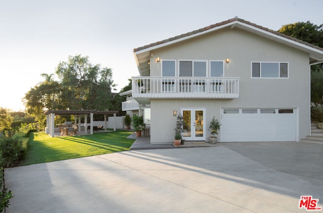 rear view of property featuring a balcony, a yard, a garage, and french doors