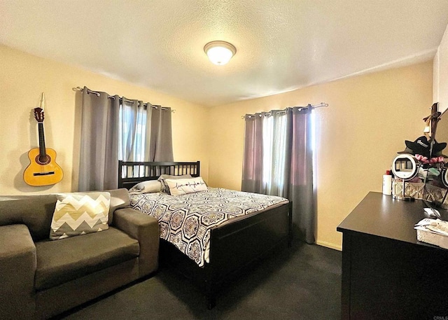 bedroom featuring a textured ceiling, multiple windows, and dark colored carpet