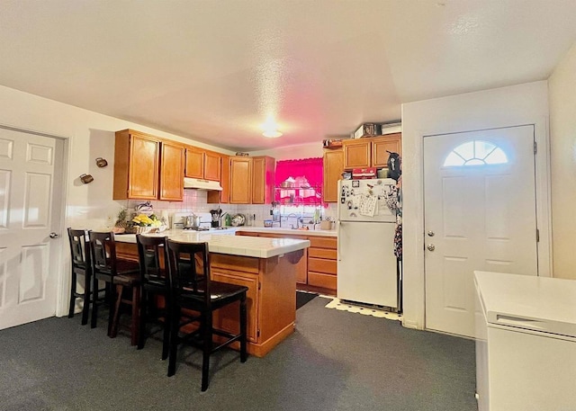 kitchen with a breakfast bar area, kitchen peninsula, tasteful backsplash, and white fridge