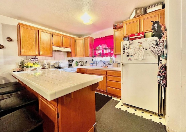 kitchen featuring white appliances, tile counters, decorative backsplash, kitchen peninsula, and a breakfast bar