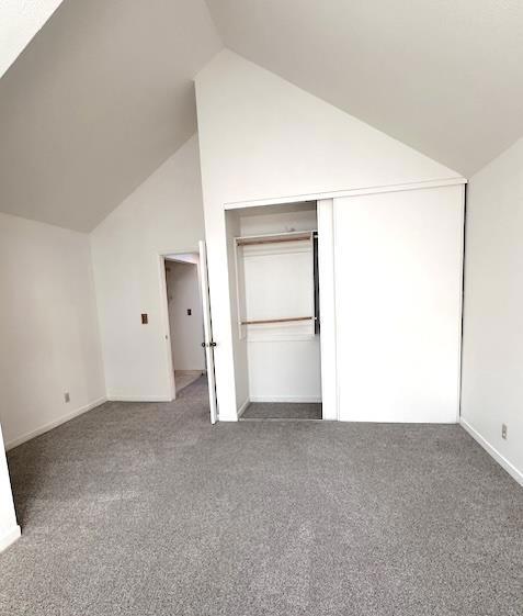 unfurnished bedroom featuring dark colored carpet, a closet, and lofted ceiling