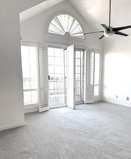 empty room with ceiling fan, plenty of natural light, carpet, and lofted ceiling