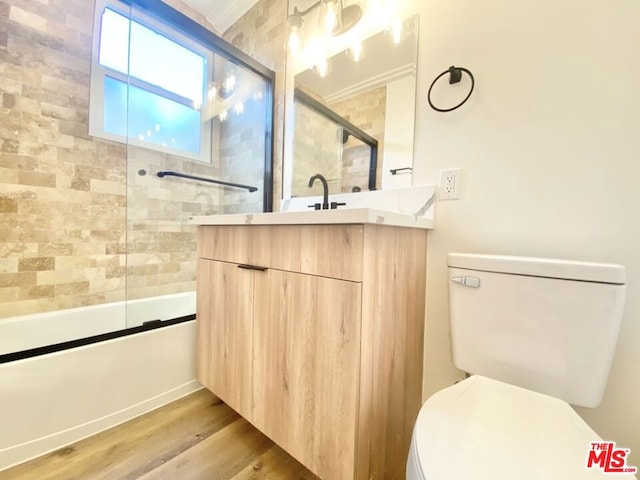 full bathroom featuring toilet, combined bath / shower with glass door, wood-type flooring, ornamental molding, and vanity