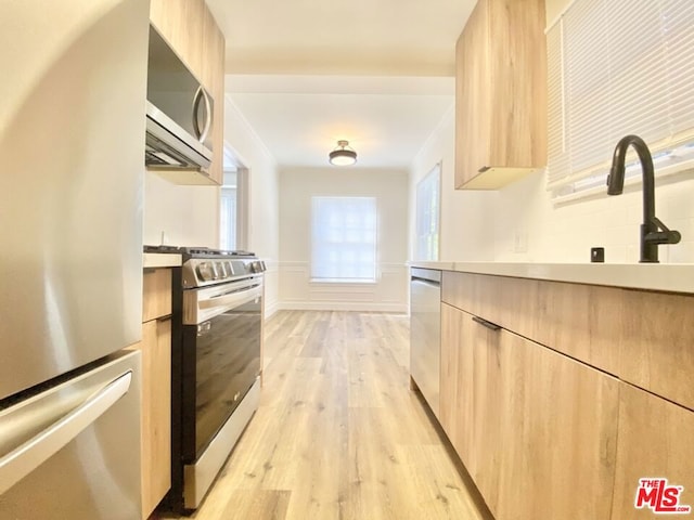 kitchen with stainless steel appliances, light brown cabinetry, light hardwood / wood-style flooring, and sink