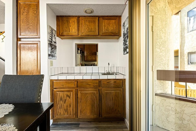 kitchen featuring a textured ceiling, dark wood-type flooring, tile counters, and sink