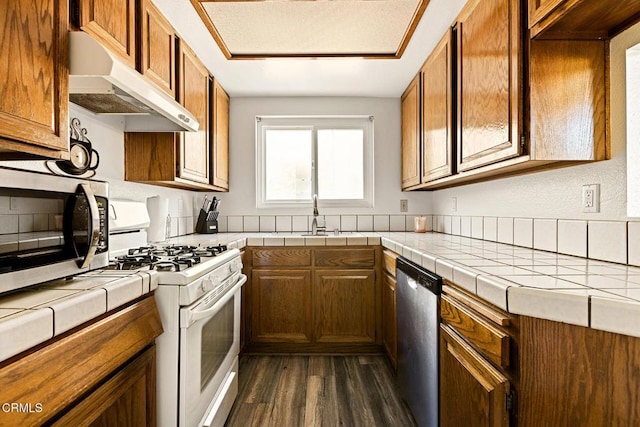 kitchen featuring stainless steel appliances, under cabinet range hood, dark wood-style floors, and brown cabinetry