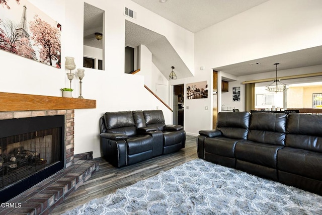 living area featuring an inviting chandelier, a fireplace, visible vents, a high ceiling, and wood finished floors