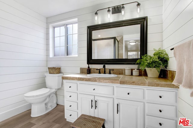 bathroom with hardwood / wood-style floors, wooden walls, toilet, and vanity