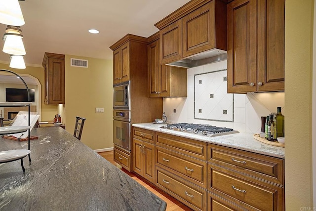 kitchen with decorative light fixtures, stainless steel appliances, dark stone countertops, backsplash, and light hardwood / wood-style flooring