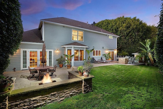 back house at dusk with french doors, a patio area, an outdoor fire pit, and a lawn