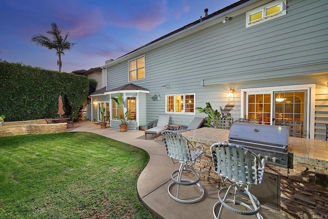 back house at dusk with a yard, a patio area, and exterior kitchen