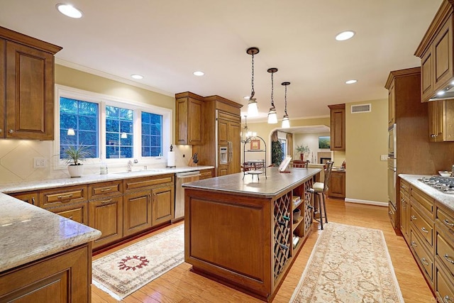 kitchen with appliances with stainless steel finishes, tasteful backsplash, a kitchen island, pendant lighting, and light hardwood / wood-style flooring