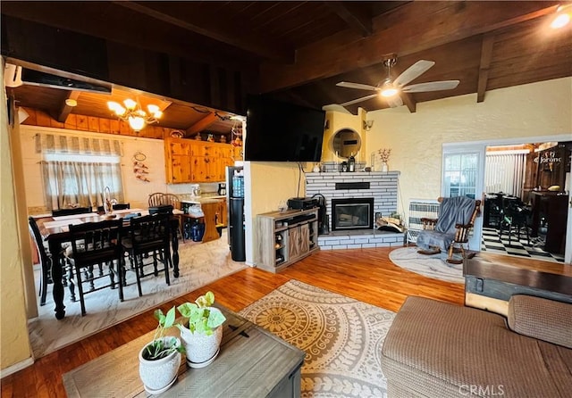 living area featuring wooden ceiling, ceiling fan with notable chandelier, wood finished floors, beamed ceiling, and a glass covered fireplace