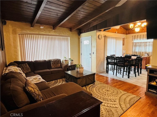 living area with a healthy amount of sunlight, light wood-style flooring, lofted ceiling with beams, and an inviting chandelier