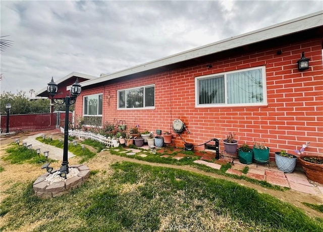 view of side of property featuring brick siding, fence, and a yard