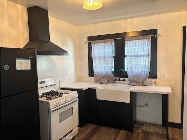 kitchen featuring wall chimney range hood, black fridge, gas range gas stove, sink, and dark hardwood / wood-style flooring