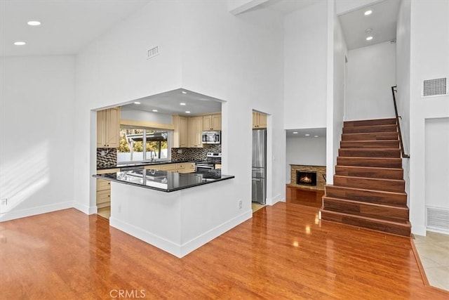 kitchen with tasteful backsplash, a fireplace, kitchen peninsula, a high ceiling, and stainless steel appliances