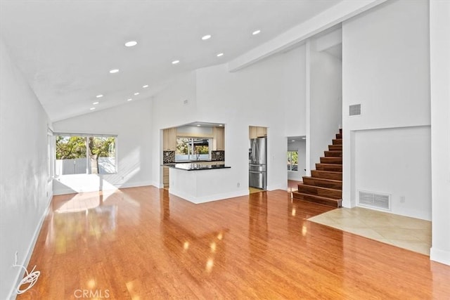 unfurnished living room featuring high vaulted ceiling and light hardwood / wood-style floors