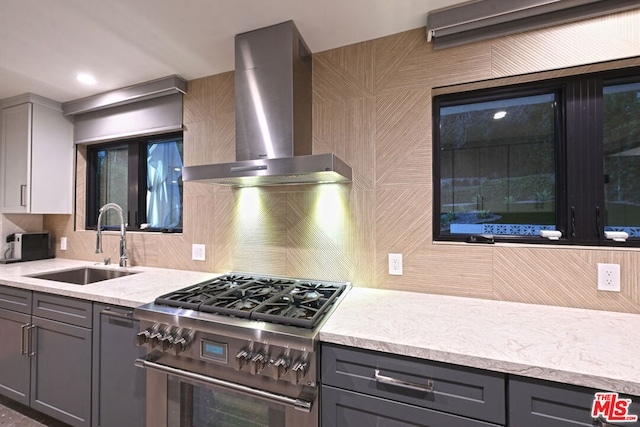 kitchen featuring stainless steel range, gray cabinetry, backsplash, wall chimney exhaust hood, and sink