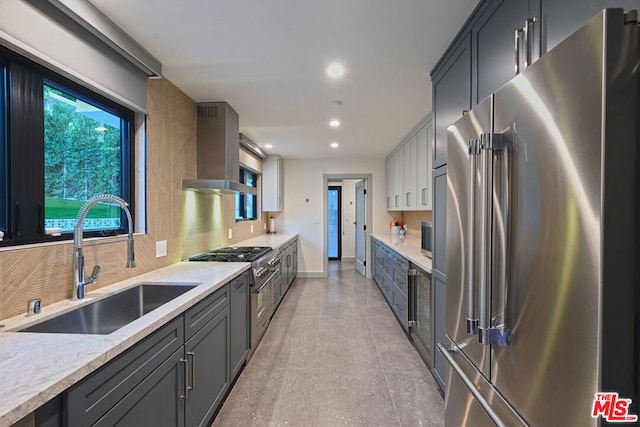 kitchen featuring sink, appliances with stainless steel finishes, gray cabinetry, wall chimney exhaust hood, and light stone counters