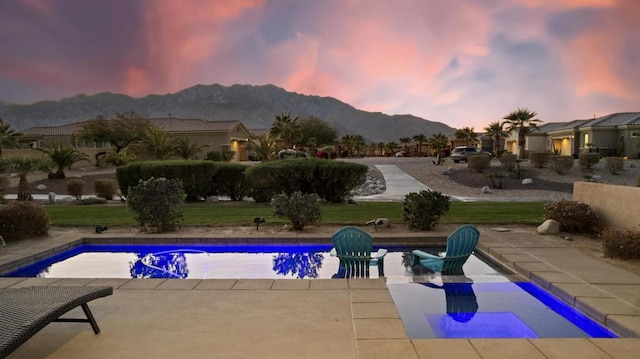 pool at dusk with a yard, a mountain view, and a patio