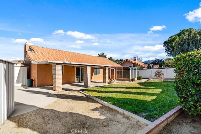 back of property with a sunroom, a lawn, and a patio