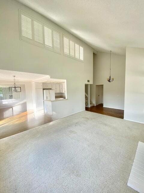 unfurnished living room featuring plenty of natural light, a textured ceiling, a notable chandelier, and carpet flooring