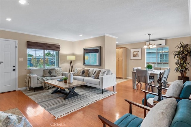 living room with ornamental molding, a wall mounted air conditioner, light hardwood / wood-style floors, and a notable chandelier