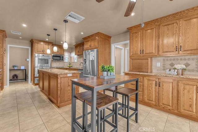 kitchen with decorative light fixtures, tasteful backsplash, light stone counters, a center island, and stainless steel appliances