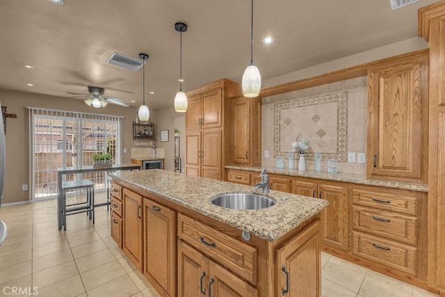 kitchen featuring decorative light fixtures, sink, light tile patterned flooring, light stone counters, and a center island with sink