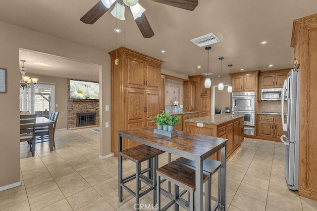 kitchen with hanging light fixtures, appliances with stainless steel finishes, light stone countertops, light tile patterned flooring, and a center island