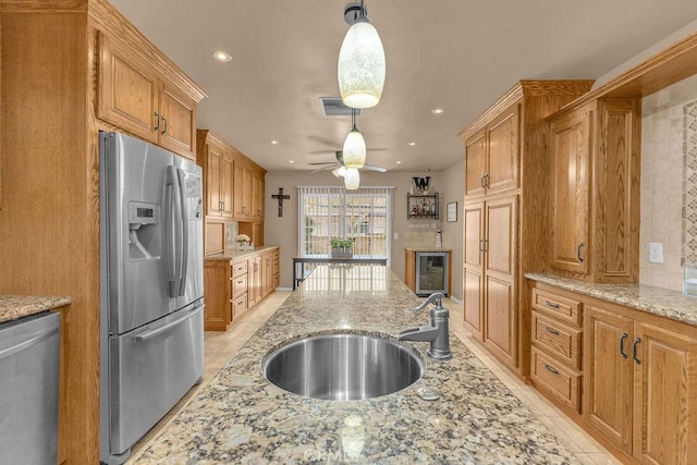 kitchen featuring ceiling fan, hanging light fixtures, sink, light stone countertops, and stainless steel appliances