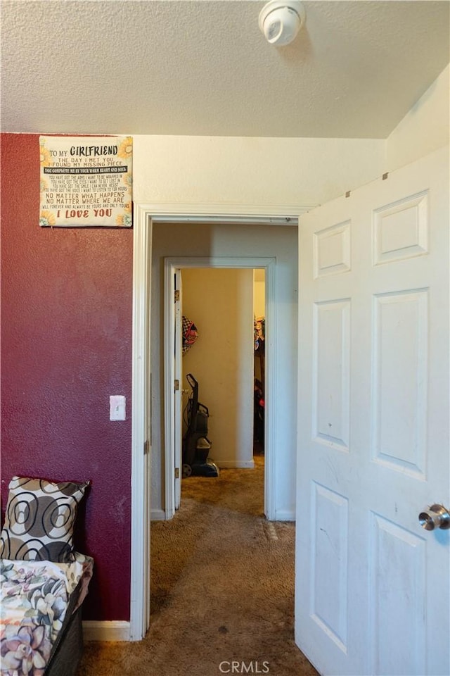 hallway featuring a textured ceiling and dark colored carpet