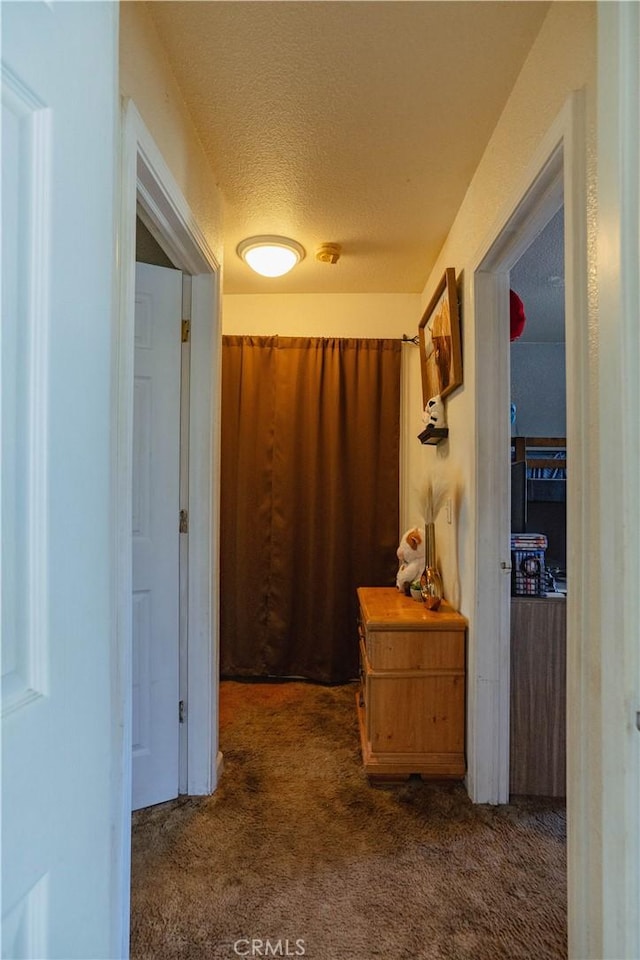 hall with a textured ceiling and dark colored carpet